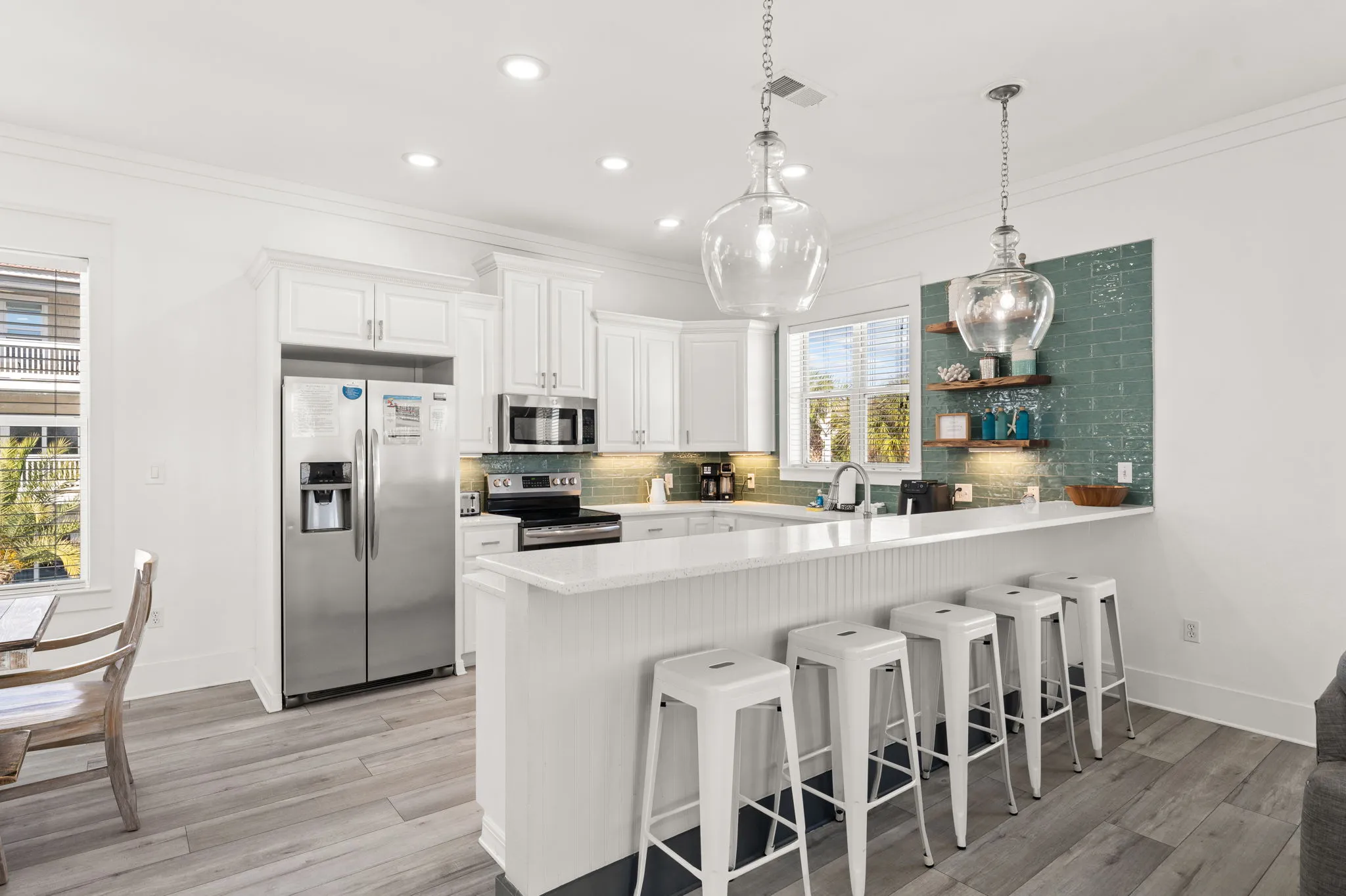 Kitchen island with bar seating, pendant lights, and teal subway tile accent wall
