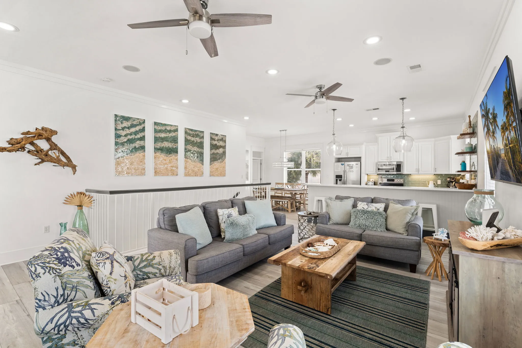 Open-concept living area with gray sectionals, coastal art, and the kitchen beyond