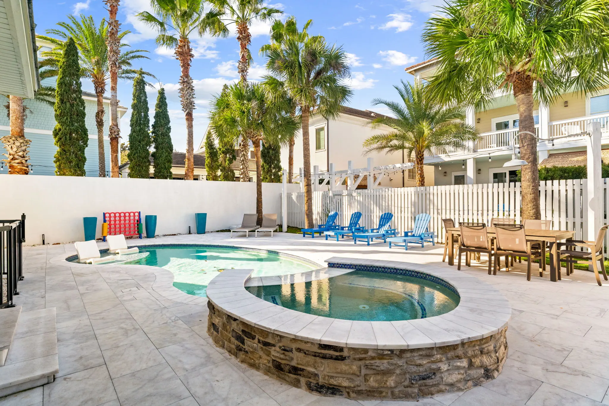 Wide backyard pool with palms, loungers, and outdoor dining
